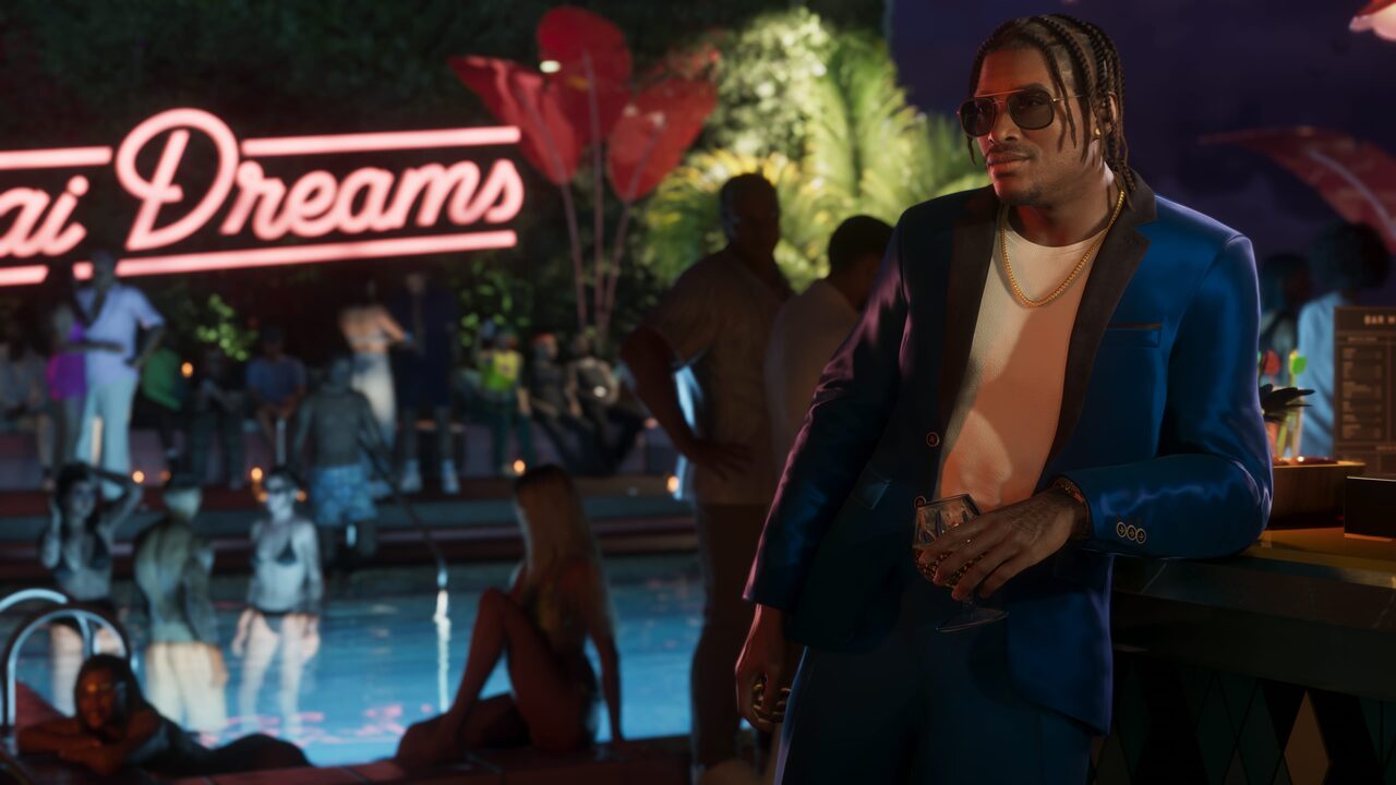 Dre'Quan Priest in a blue blazer holding a drink beside a poolside bar at night, a neon sign behind him.