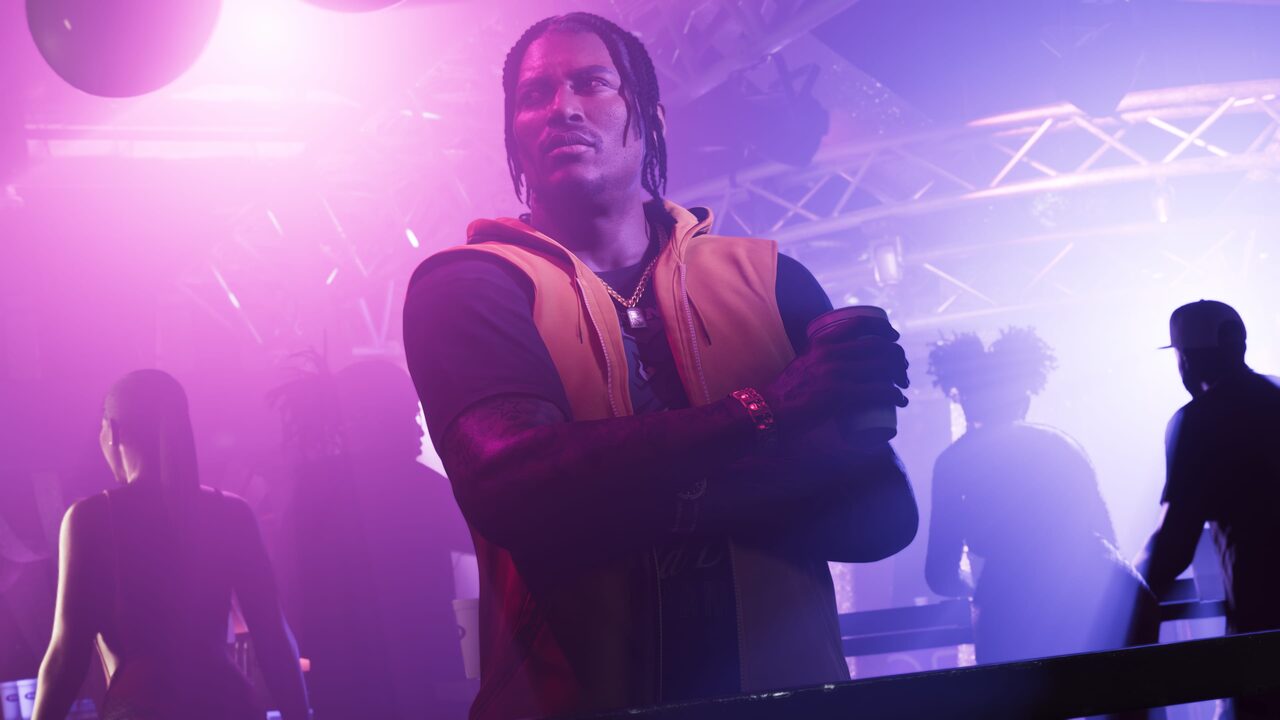 Dre'Quan Priest standing with arms crossed in a nightclub, colored lights and other figures behind him.