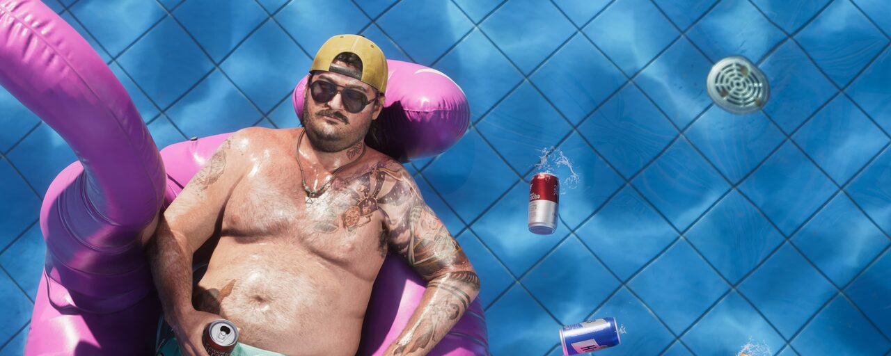 A shirtless, tattooed man in sunglasses and a backwards cap lounging in a pink inflatable ring in a pool, holding a can, with more cans floating nearby.