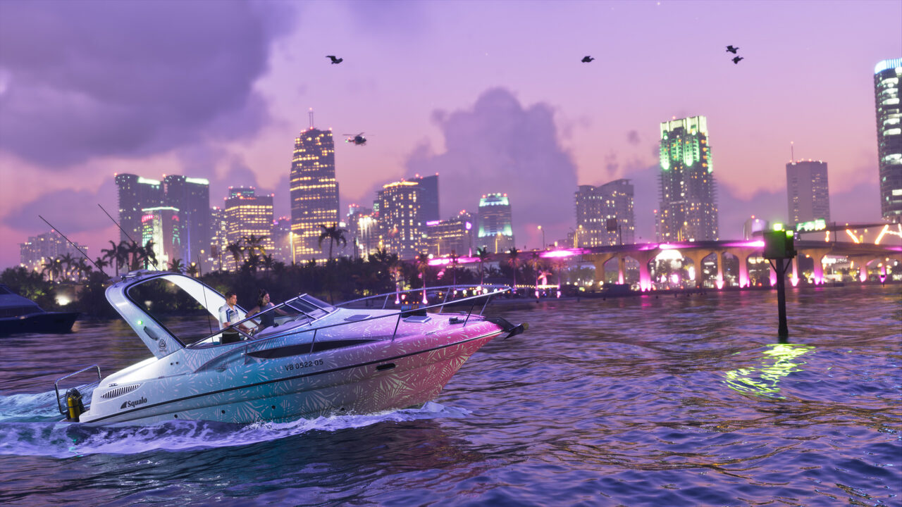 A Squalo speedboat with a pink and teal patterned hull crossing open water at dusk, a lit city skyline and a pink-lit causeway behind it.