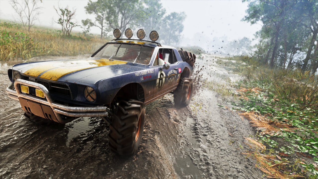 A blue and yellow race-liveried muscle car raised on knobbly off-road tyres, throwing mud as it powers along a wet dirt track.