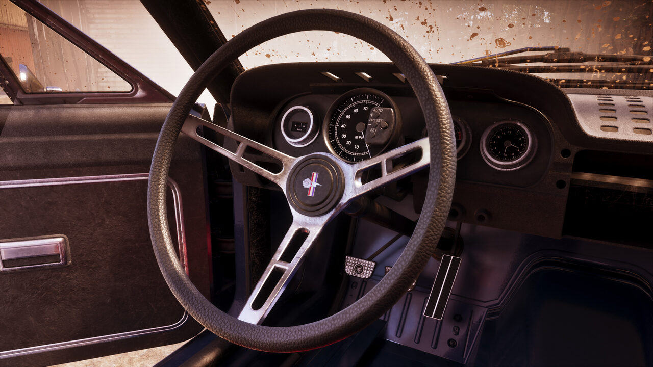 The interior of a stripped classic muscle car, a three-spoke steering wheel and simple round gauges seen through a mud-flecked windscreen.