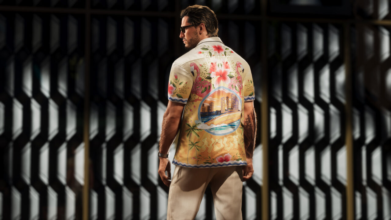 A man seen from behind in a cream camp shirt printed with flamingos, hibiscus and a beach-skyline scene, standing before a dark slatted wall.
