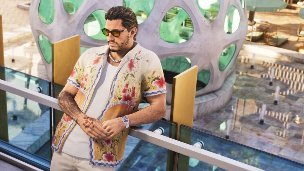A man in a floral camp shirt and sunglasses leaning on a glass balcony rail above a pool deck, a green perforated sculpture behind him.