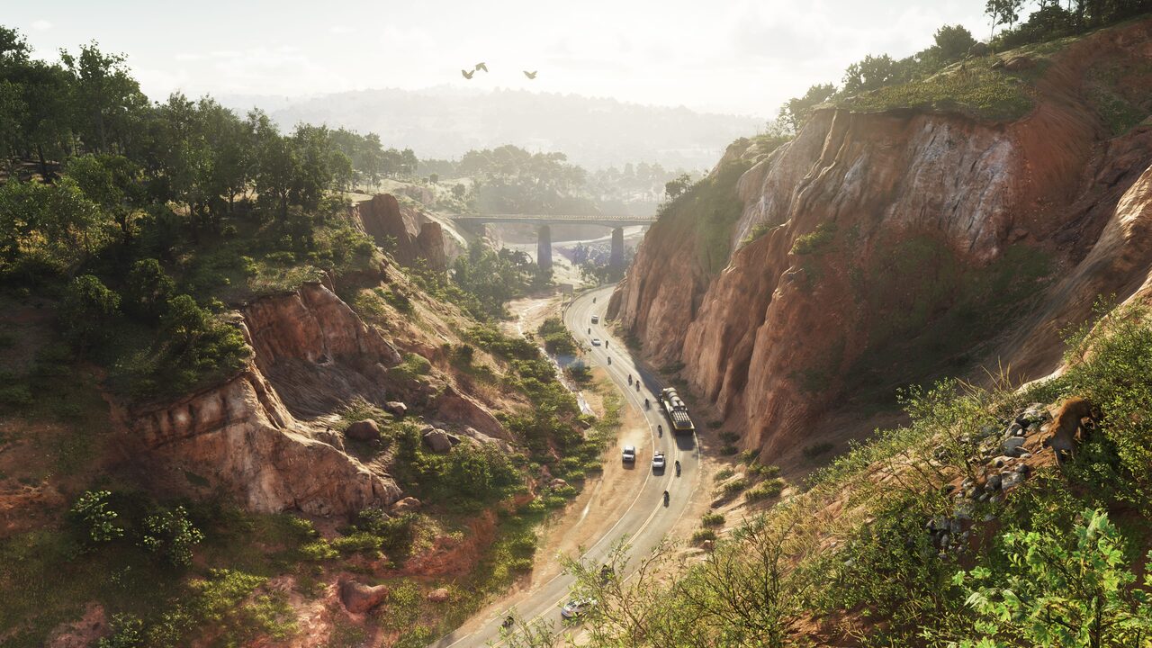 A two-lane road winding through a cut in red rock bluffs, traffic strung along it and a bridge crossing the gap ahead.