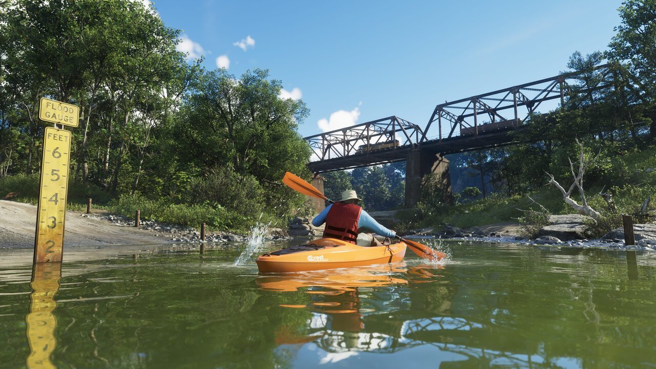 A kayaker paddling a green river toward a steel truss railway bridge, a yellow flood gauge marked off in feet standing in the water at the left bank.