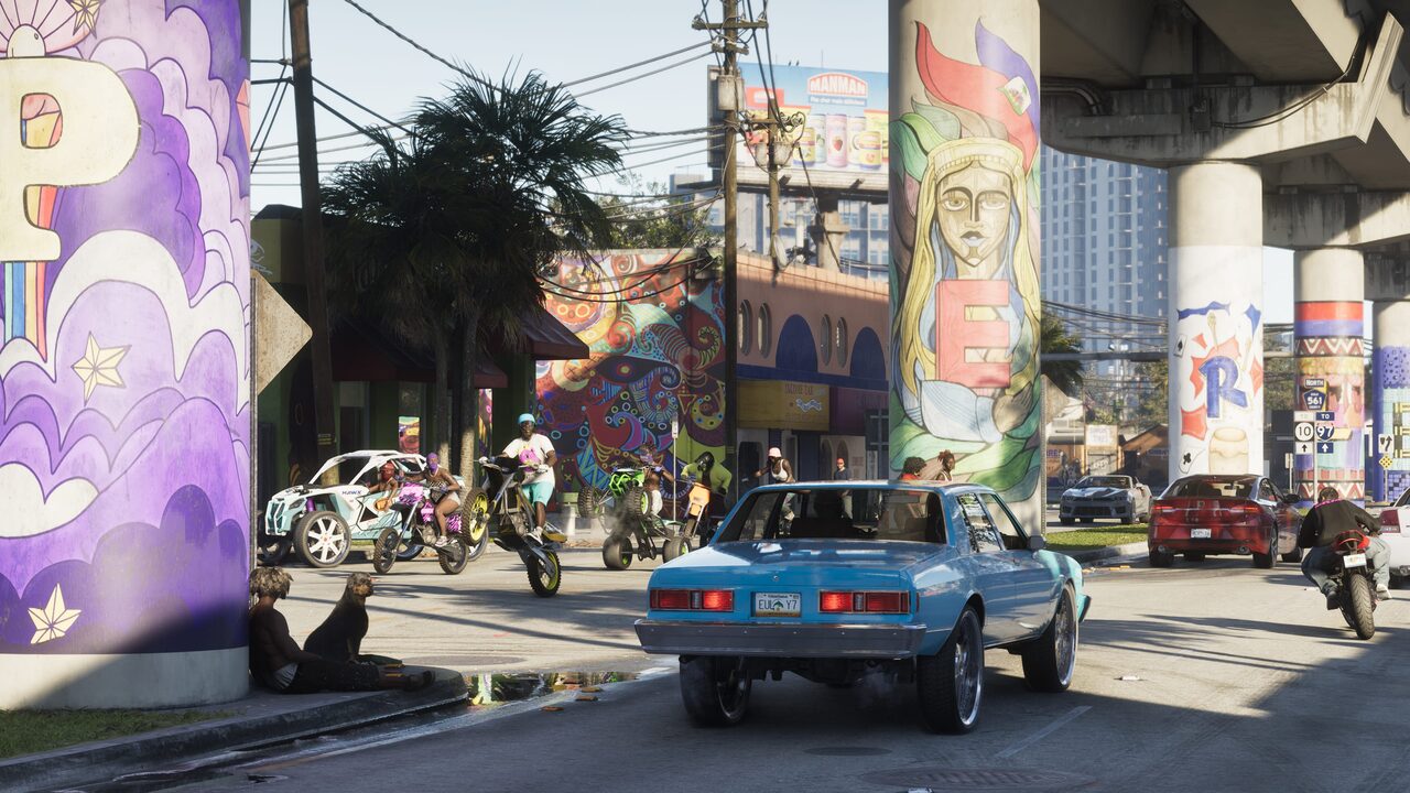 A sedan waiting at an underpass junction, the flyover columns painted with murals and dirt bikes wheelieing across the intersection ahead.